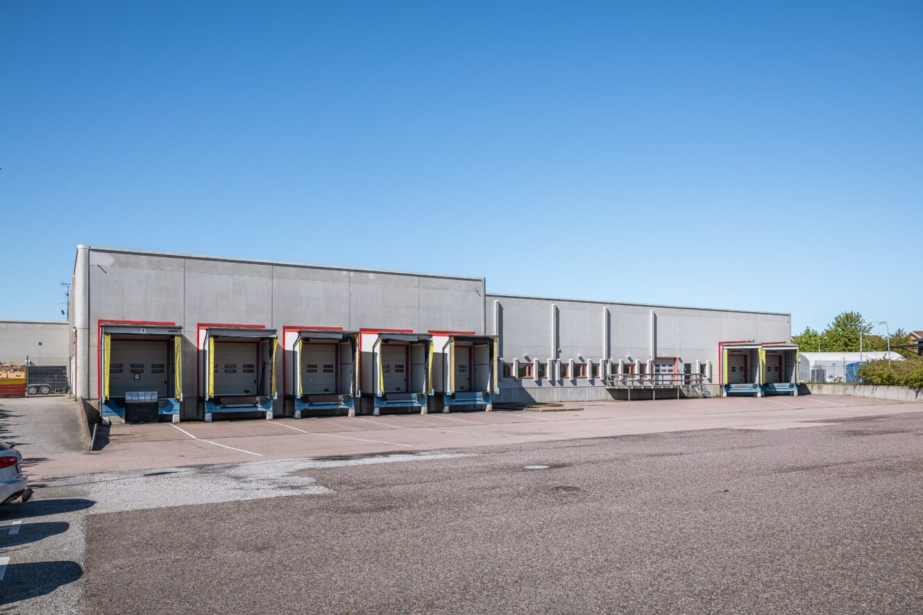 Ett lager med fem lastkajer, var och en med en stängd takskjutport, omgiven av en tom asfalterad tomt under en klarblå himmel.