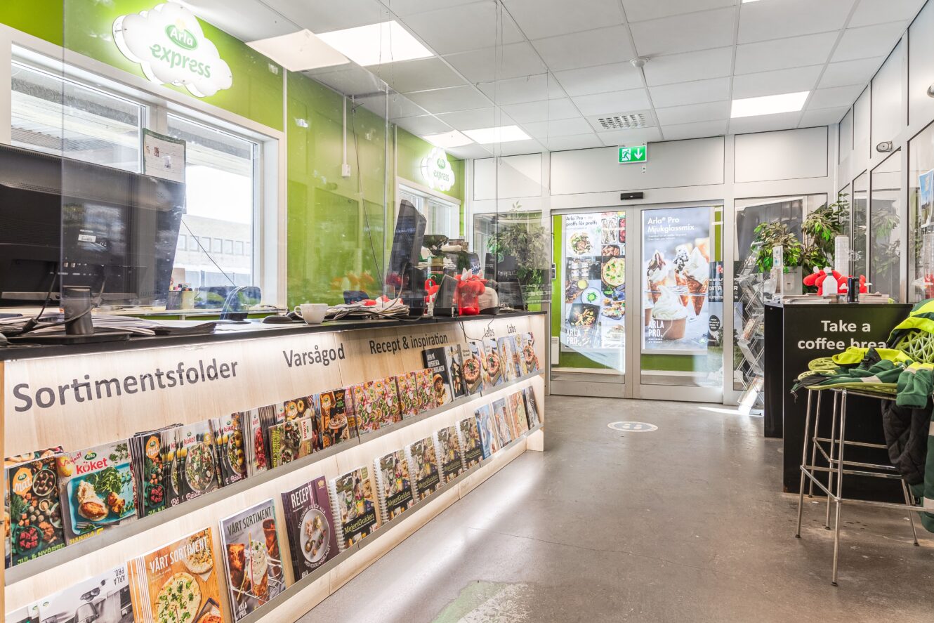 En ljus butiksinredning med en utställning av kokböcker på en disk, gröna väggar och en kaffestation nära ingången.