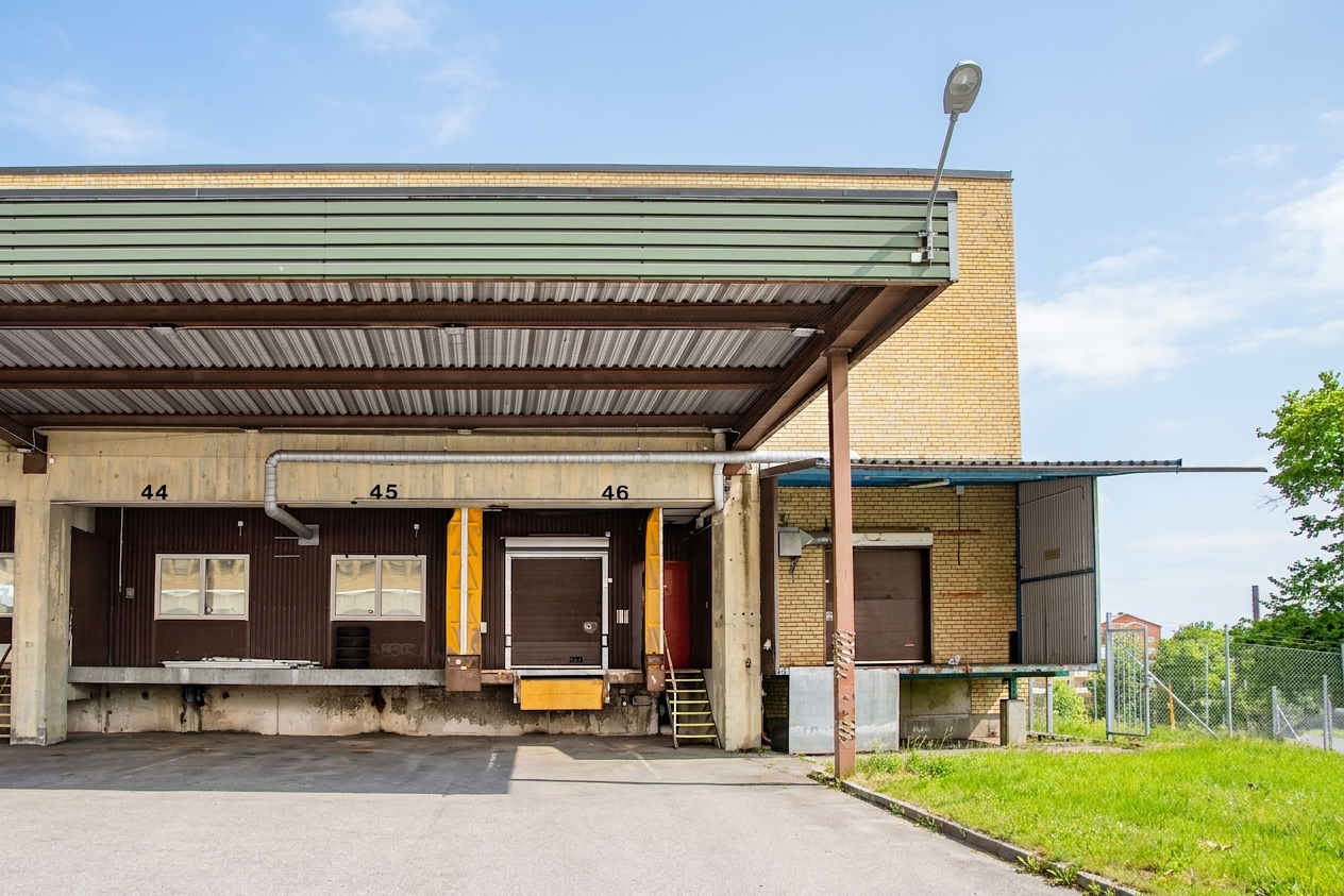 Tre lastkajer med numren 44, 45 och 46 vid en lagerbyggnad med metallmarkiser ovanför och en gatlykta framför. Till höger syns gräs och ett staket.
