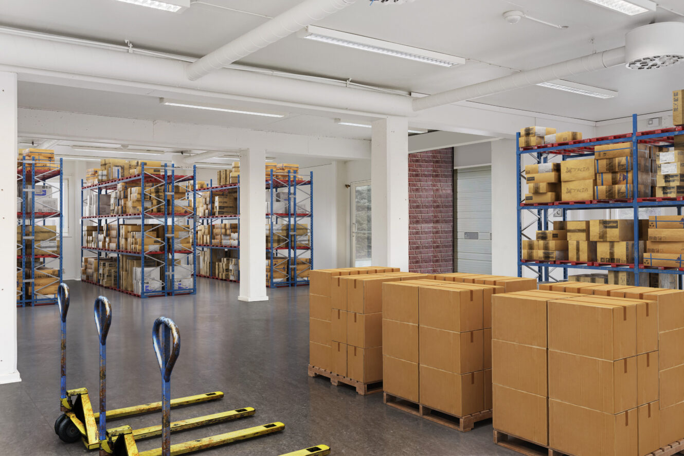 En lagerlokal med staplade kartonger, metallhyllor fyllda med kartonger och tre gula pallbockar på golvet.