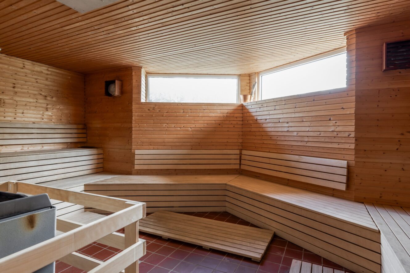 Tomt basturum i trä med bänkar i flera nivåer, ett aggregat i hörnet och fönster nära taket som släpper in naturligt ljus.