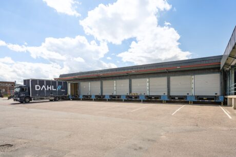 En lastbil med DAHL-märke står parkerad vid en lastkaj med flera stängda dörrar en solig dag.