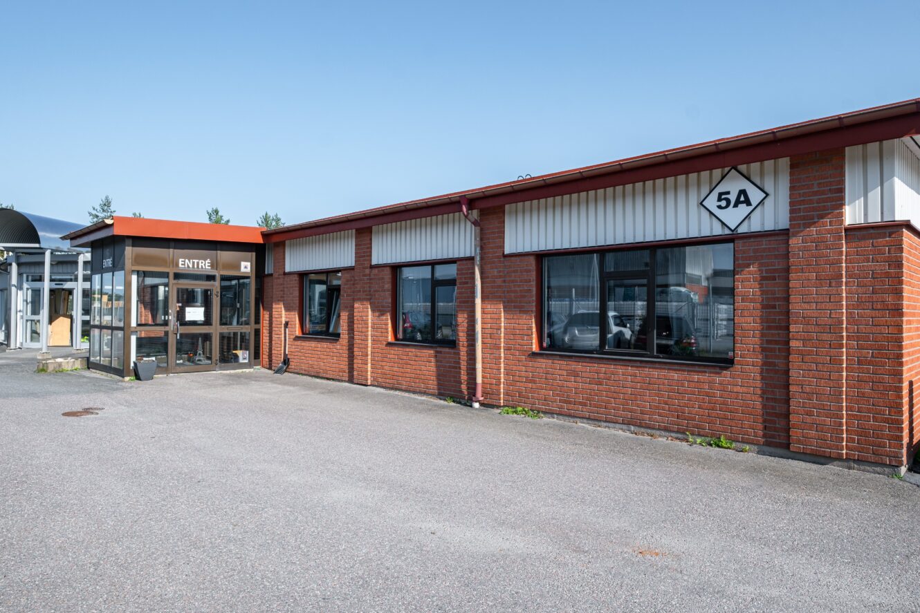 Envånings affärsbyggnad i tegel med stora fönster, en glasentré märkt ENTRÉ och en skylt som visar 5A på fasaden; klar himmel ovanför.