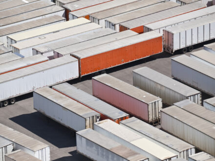 Flygfoto över rader av parkerade containrar och släpvagnar på en parkeringsplats, de flesta vita med några röda och orange.