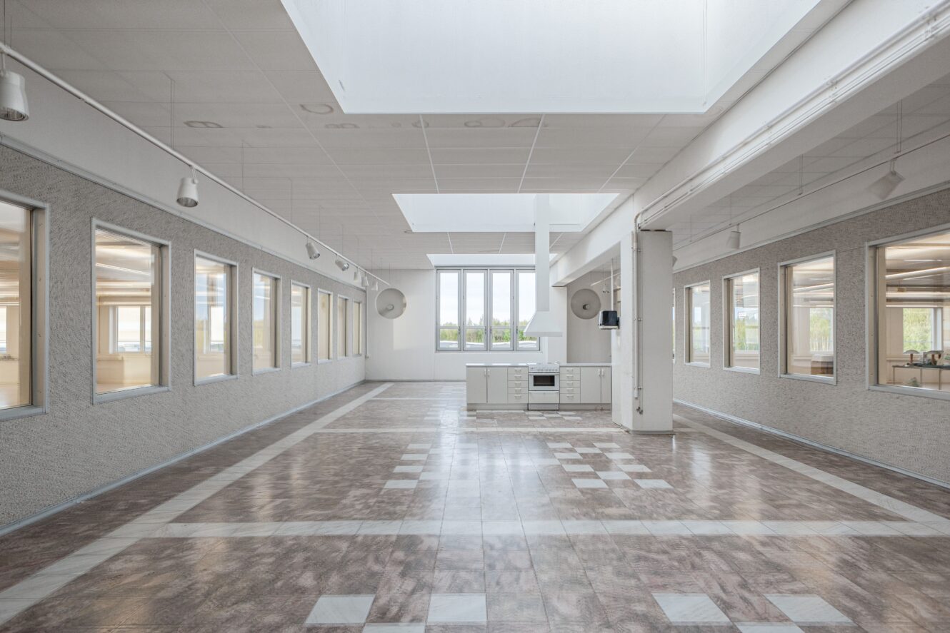 Rymligt, tomt rum med klinkergolv, stora fönster på båda sidor, takfönster ovanför och ett litet pentry längst bort.