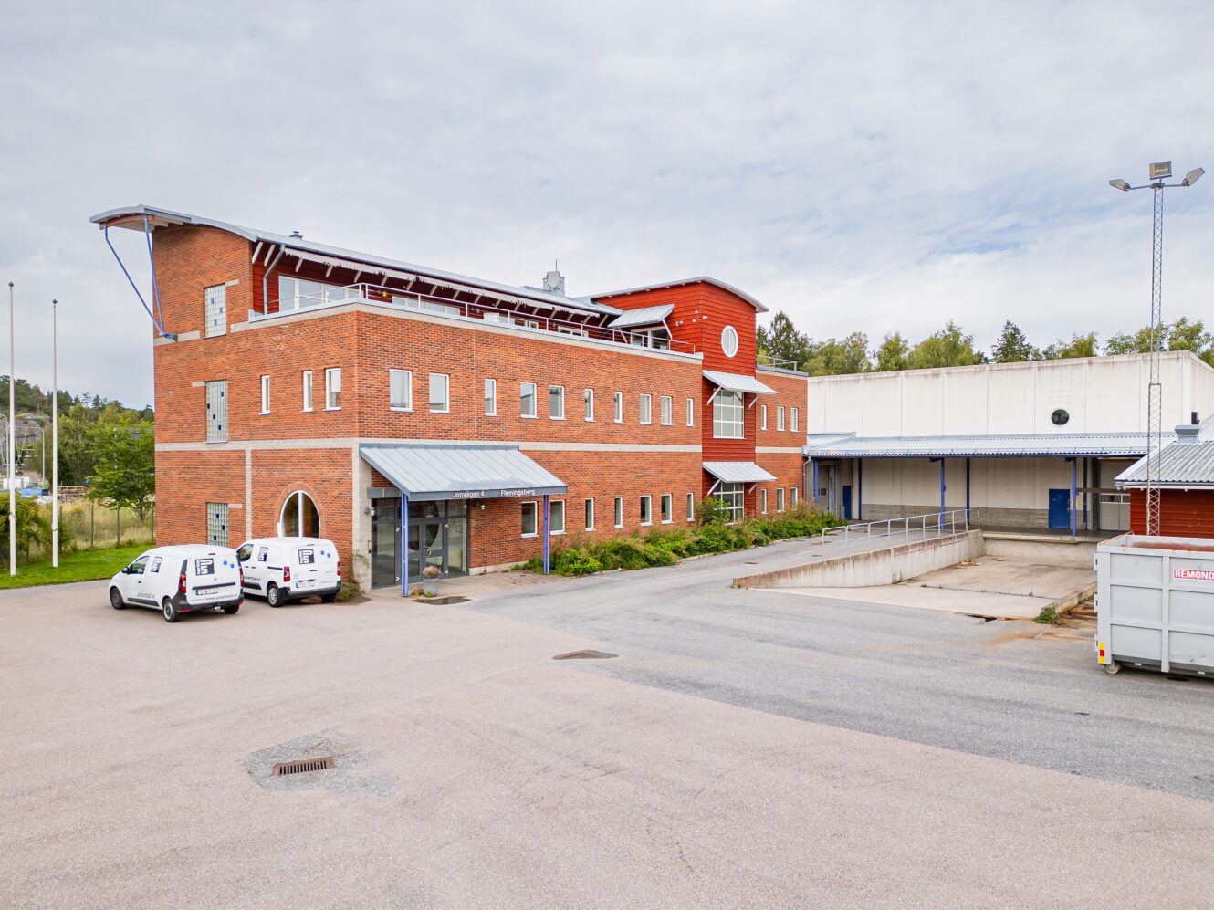 En modern kommersiell byggnad i tegel och metall med skåpbilar parkerade utanför och en lastkaj synlig till höger.