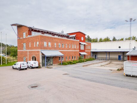 En modern kommersiell byggnad i tegel och metall med skåpbilar parkerade utanför och en lastkaj synlig till höger.