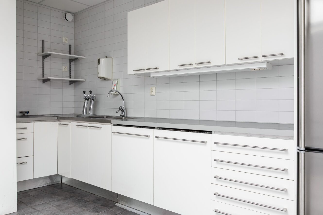 Ett modernt kök med vita skåp, handtag i rostfritt stål, diskho, väggmonterade hyllor och kaklat stänkskydd.