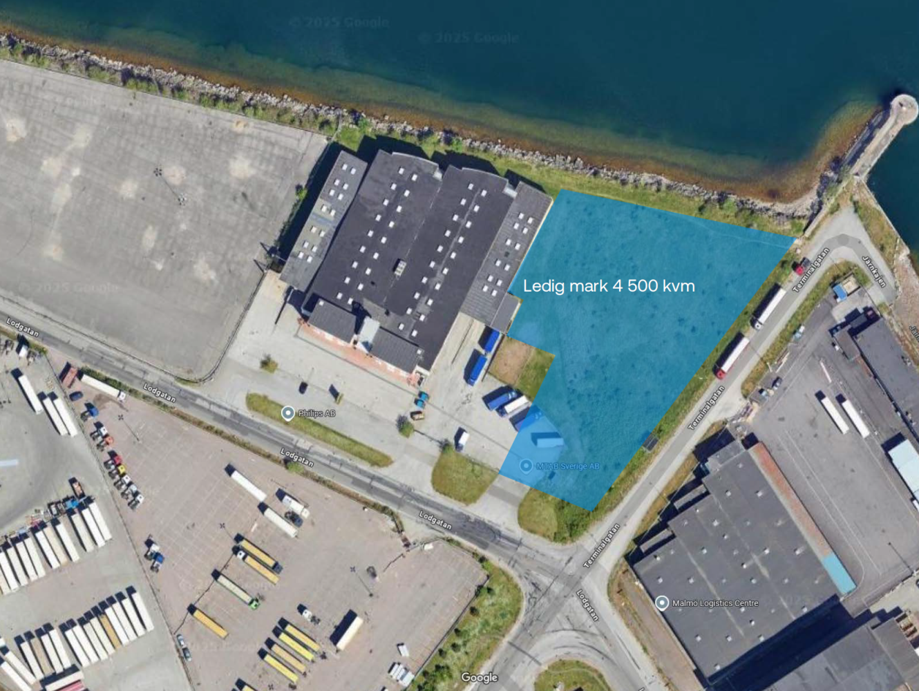 Flygfoto över ett industriområde vid vattnet, med en ledig tomt märkt Ledig mark 4 500 kvm i blått bredvid en stor byggnad.