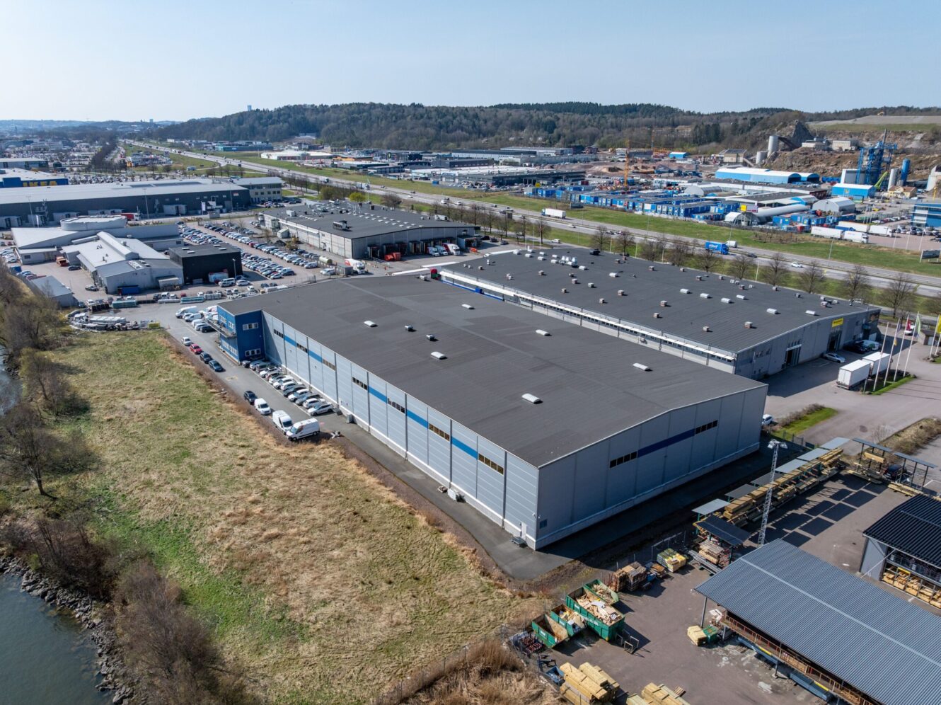 Flygfoto över ett stort industriellt lagerkomplex med omgivande parkeringsplatser, vägar och intilliggande byggnader i ett affärsdistrikt.