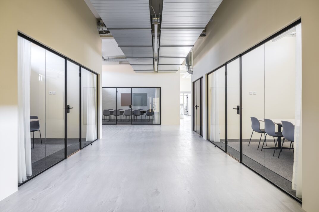 En modern kontorskorridor med mötesrum med glasväggar på båda sidor och ett konferensrum som syns i slutet.