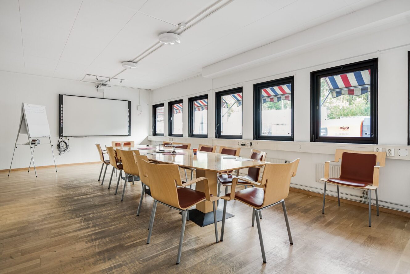 Ett modernt konferensrum med ett långt bord, trästolar, whiteboard, blädderblock och stora fönster med randiga markiser.