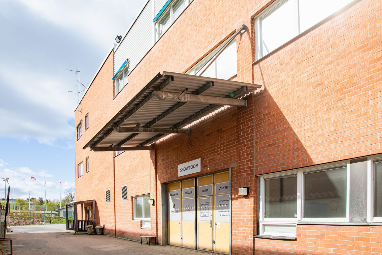 En tegelbyggnad med en metallmarkis över dubbeldörrar märkta SHOWROOM; fönster och en klar himmel syns.