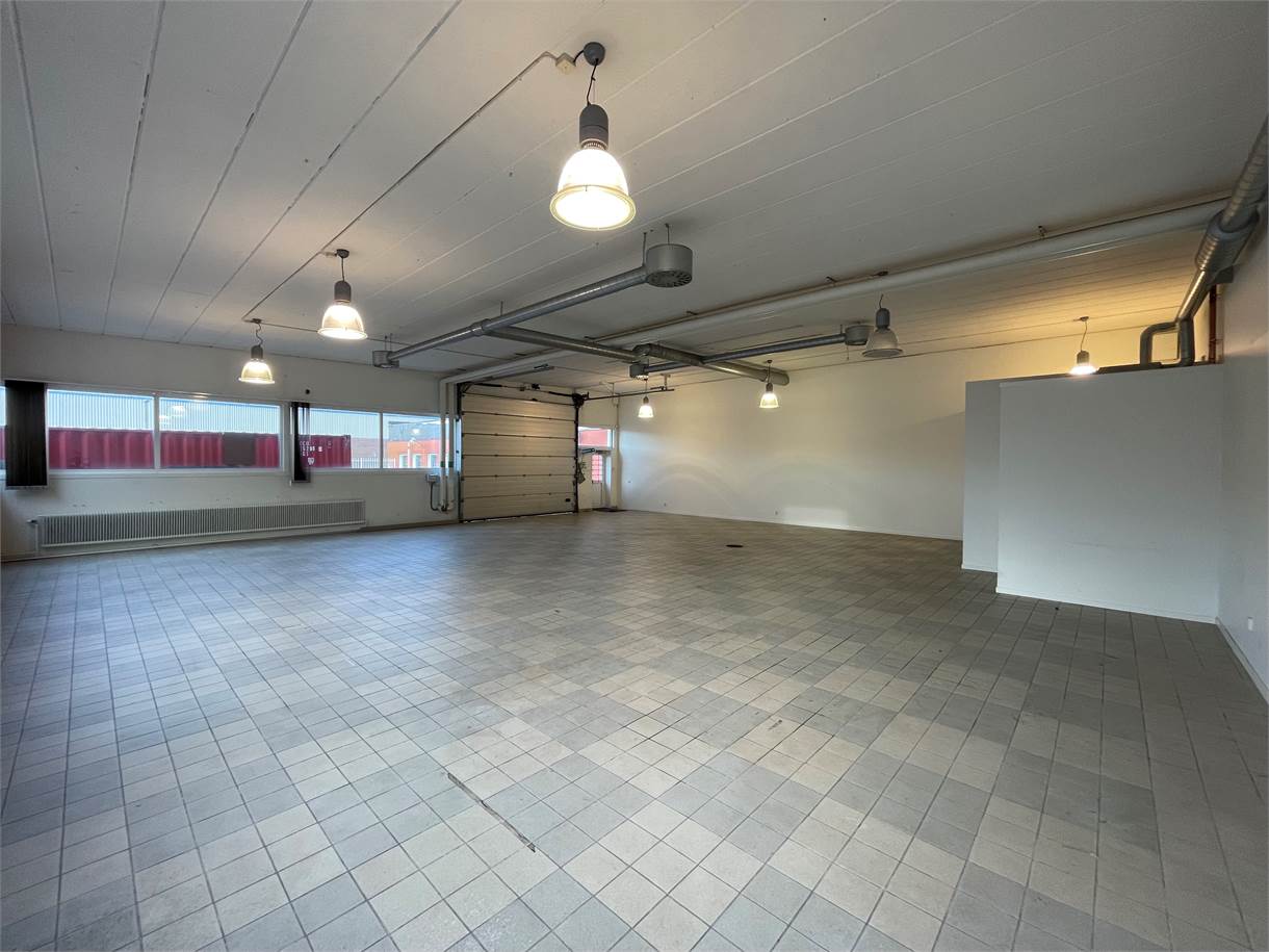 Rymligt, tomt industrigarage med klinkergolv, takbelysning, stora fönster och en rullport.