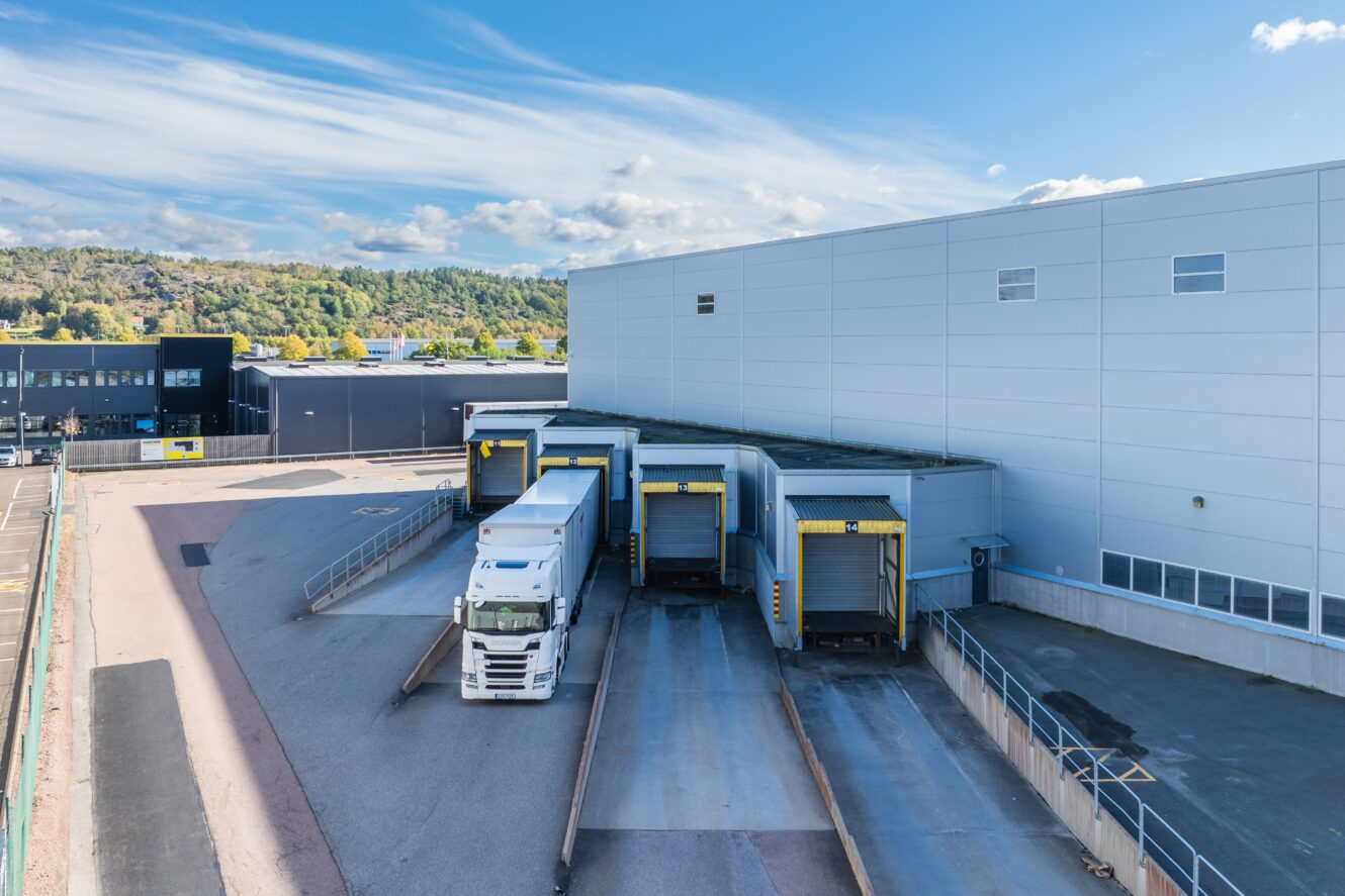 En vit semitrailer står parkerad vid en lastkaj i ett stort industrilager en klar dag, med flera lastkajer synliga.