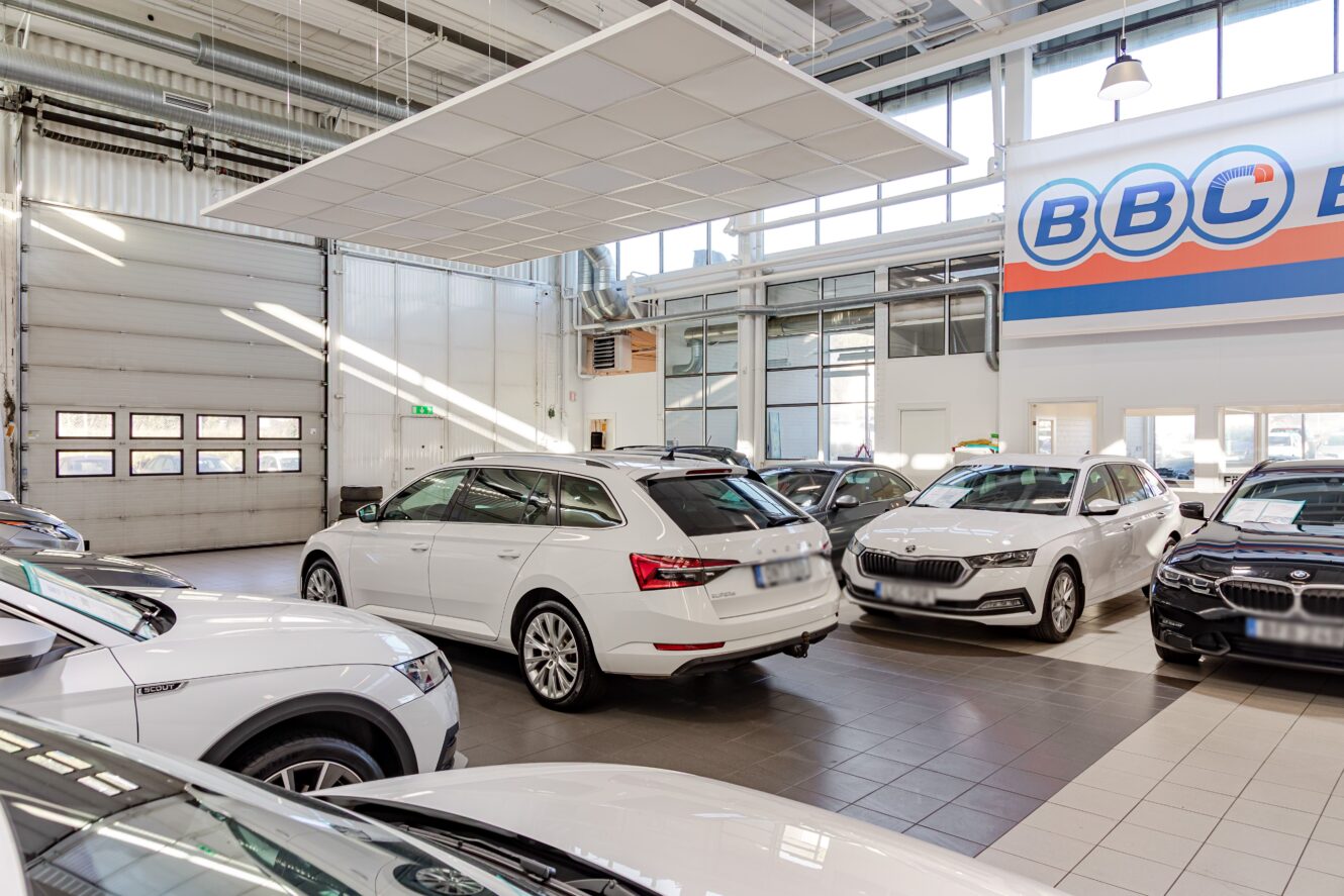 En bilhandlares utställningslokal med flera vita och svarta bilar parkerade inomhus under stora fönster och taklampor.