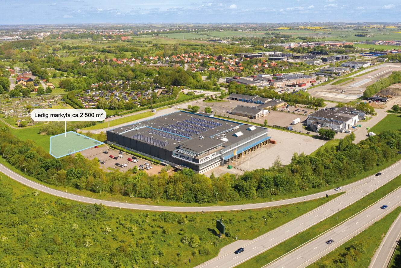 Flygfoto visar en industribyggnad med en markerad 2.500 m² stor ledig yta i närheten, omgiven av grönska och vägar.