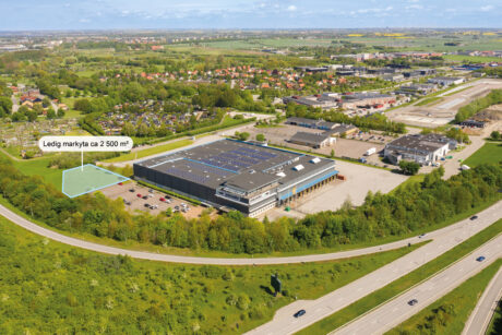 Flygfoto visar en industribyggnad med en markerad 2.500 m² stor ledig yta i närheten, omgiven av grönska och vägar.