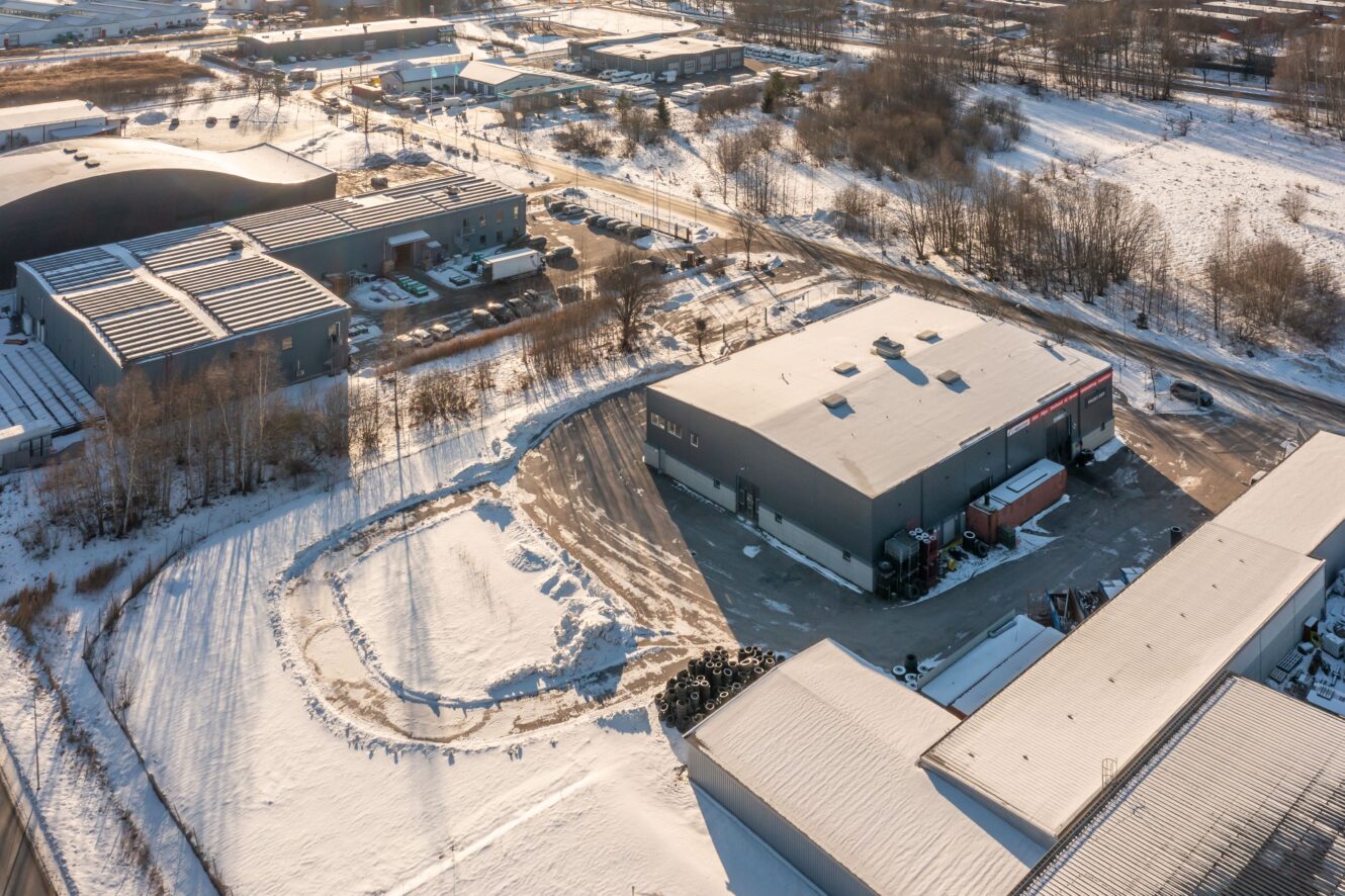 Flygfoto över industribyggnader och lagerlokaler omgivna av snö i ett kommersiellt område under vintern.