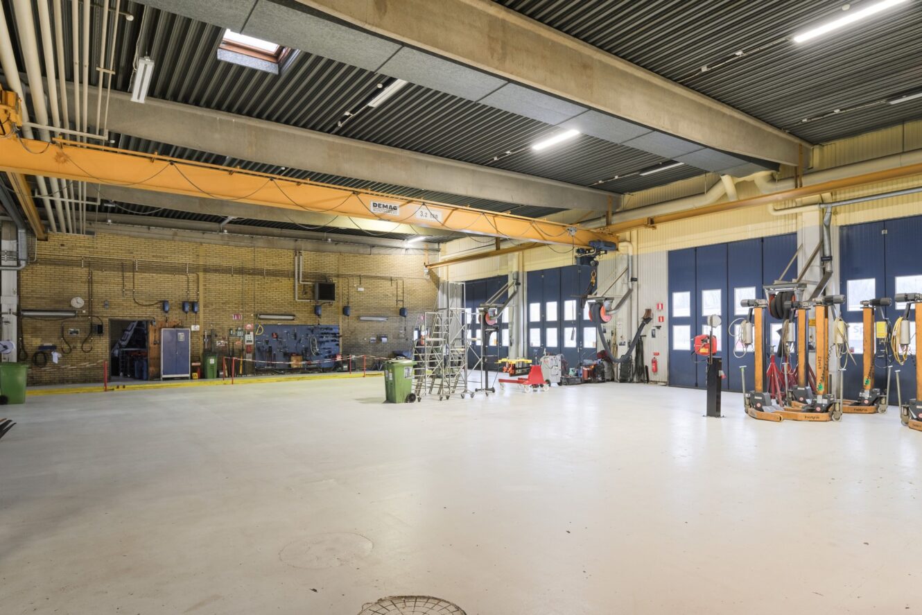 Rymlig industriverkstad med högt i tak, arbetsstationer, diverse utrustning och verktyg prydligt uppställda längs väggarna.